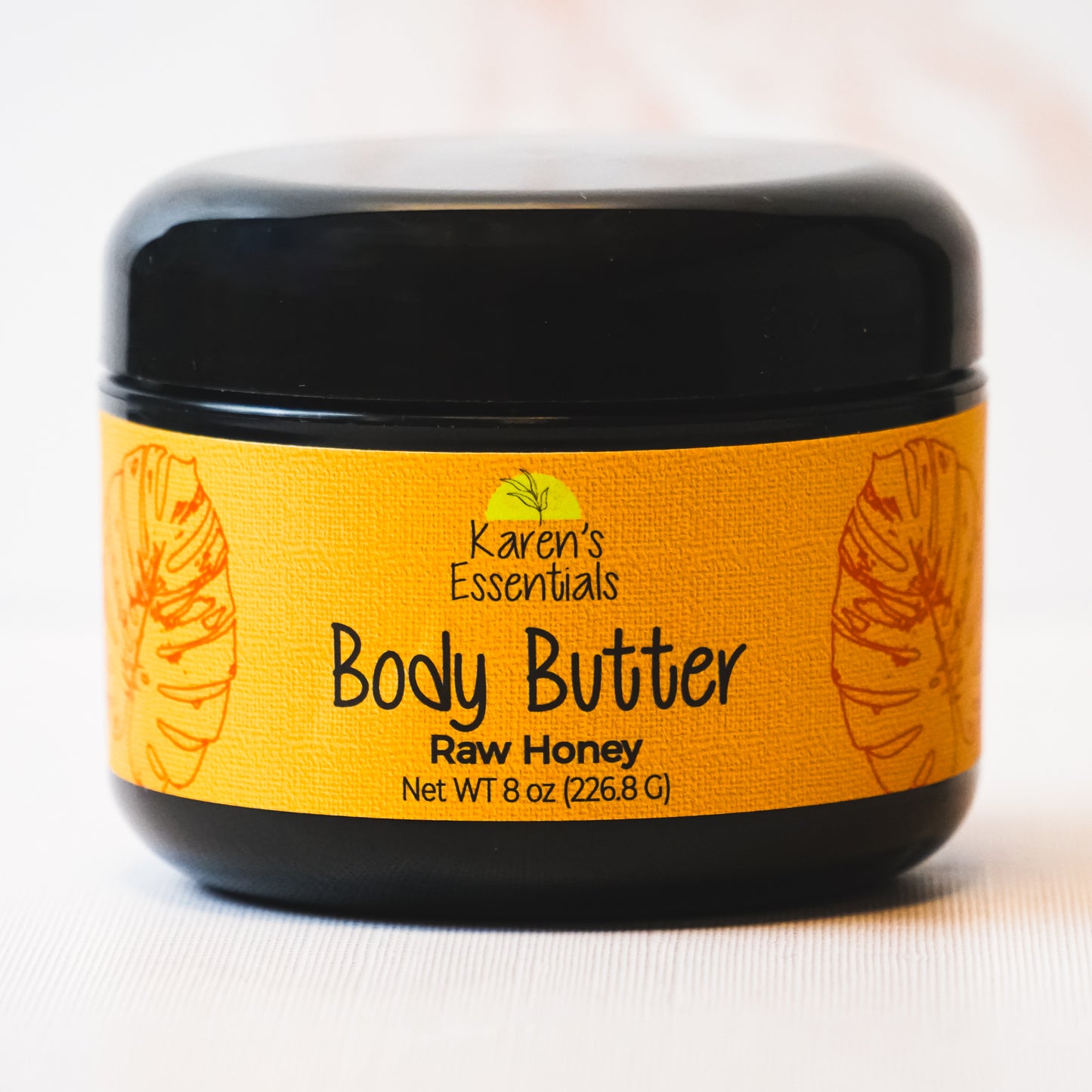 picture of a black container featuring a gold label with black text stating Karen Essentials, the company name, the container is Body Butter with the scent of Raw Honey in a 8 oz container 